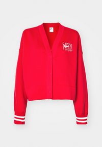 Röd kort kofta med V-ringning, ribbade muddar med vita ränder och en Nike-logotyp på vänster bröst. Tillverkad av mjukt tyg.