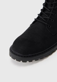 Μαύρη σουέντ μπότα αστραγάλου με στρογγυλή μύτη, κορδόνια στο μπροστινό μέρος, υφή επιφάνειας και χοντρή, ανθεκτική ε�λαστική σόλα με βαθιά ανάγλυφη επιφάνεια.