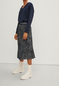 Sweatshirt con scollo a V blu navy con logo casual, abbinato a una gonna midi a campana bianco e nera a fantasia e stivaletti crema con suola spessa.