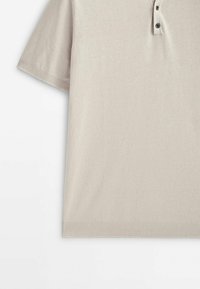 Polo beige à manches courtes avec ourlet et poignets côtelés, présentant une patte de boutonnage à trois boutons au col.