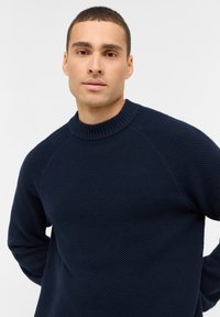 Marineblaue Strickjacke mit einem gerippten Rundhalsausschnitt, strukturiertem Stoff und Raglanärmeln. Enganliegendes Design.