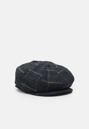 Donkerblauwe platte pet met een geruit patroon in beige lijnen, weergegeven op een effen lichtgrijze achtergrond.