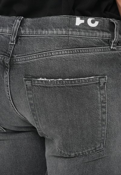 Svarta denimjeans med en blekt gråtvätt, med en bakficka, vitt logotyp på midjebandet och slitna detaljer vid kanterna.