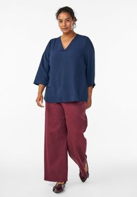 Haut bleu marine à manches trois-quarts avec un décolleté en V, associé à un pantalon bordeaux à jambes larges et des mocassins noirs brillants.