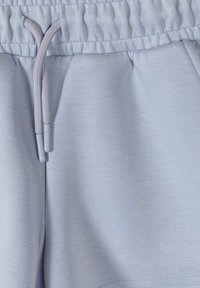 Gros plan sur un pantalon de survêtement bleu clair montrant une taille élastique avec cordon de serrage et la texture douce du tissu en coton.