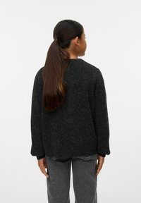 Übergroßer schwarzer Pullover aus strukturiertem Strickmaterial, mit Rundhalsausschnitt und überschnittenen Schultern, getragen mit grauen Hosen.