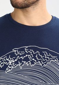 Navy blue cotton t-shirt featuring a white graphic design of a wave and stylized lines resembling ocean waves across the fabric.