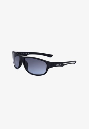 Occhiali da sole avvolgenti neri con lenti scure sfumate e logo bianco Guess sulle aste, mostrati su sfondo bianco.