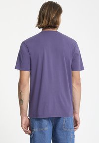 Lila Baumwoll-T-Shirt mit kurzen Ärmeln und Rundhalsausschnitt. Es verfügt über eine glatte Textur und eine lockere Passform, von hinten betrachtet.