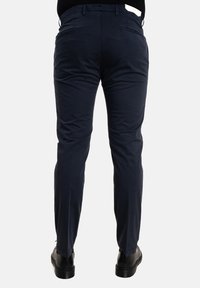 Pantaloni blu navy con una vestibilità slim, dotati di tasche laterali e una texture liscia. Un paio di scarpe nere sono visibili in basso.