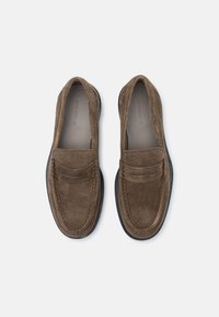 Braune Wildleder-Slipper mit strukturiertem Vorderblatt, genähten Details und einer kontrastierenden schwarzen Gummisohle. Klassisches Slip-On-Design.