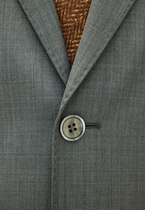 Grijze getextureerde blazer dichtgeknoopt over een bruine gebreide trui met patroon, met zichtbare revers en enkele knoopdetail.