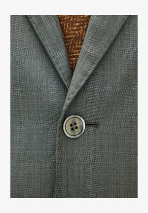 Grauer strukturierter Blazer, zugeknöpft über einem braunen, gemusterten Pullover, mit sichtbarem Revers und Ein-Knopf-Detail.
