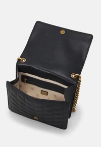 Sort quiltet læder skuldertaske med guldkæde, der har et beige indre og en lynlåslomme, sikret med en trykknapslukning.