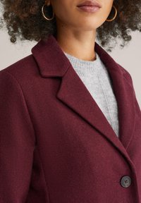 Burgundský vlněný blazer s klopovým límcem, zapínáním na jeden knoflík a jemnou texturou, nošený přes světle šedý pletený svetr.