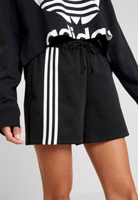 Černé šortky s hladkou texturou, s bílými trojitými pruhy na bocích a stahovací šňůrkou v pase.