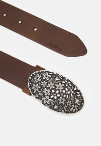 Brown leather belt with an oval silver buckle featuring an embossed floral design. The end of the belt is tapered, showing the brand engraving.