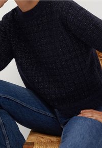 Maglione lavorato a maglia blu navy con un motivo texture, scollatura rotonda e dettagli con frange all'orlo, abbinato a jeans blu.