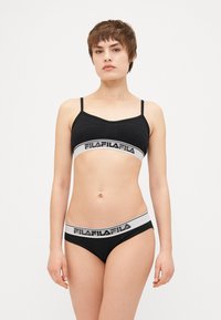 Bralette preta com alças ajustáveis, apresentando uma faixa branca com letra preta; cueca preta combinando com um design semelhante na faixa.