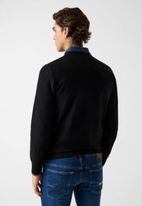 Schwarzer Strickpullover mit Rundhalsausschnitt, strukturierter Oberfläche und gerippten Bündchen, kombiniert mit blauen Jeans aus Denim mit Gesäßtaschen.