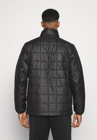 Zwarte pufferjack met een gestikt ontwerp, hoge kraag en lange mouwen. Gladde, glanzende textuur met een relaxte pasvorm.