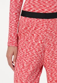 Red and white patterned fitted top with long sleeves, featuring a black elastic waistband and textured fabric, showcasing a sporty design.