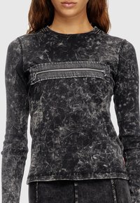 Tricou cu mânecă lungă de culoare neagră, cu un finisaj texturat, spălat cu acid. Dispune de un buzunar cu fermoar pe piept și mansete cu model canalé.