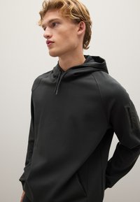 Felpa con cappuccio grigio scuro, dotata di tasca con zip sul braccio sinistro, con una texture liscia e maniche raglan per una vestibilità comoda.