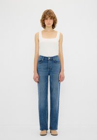 Jeans in denim blu a vita alta con una vestibilità dritta, dotati di cinque tasche, accessori in tonalità oro e una leggera scoloritura. Abbinate a una canotta bianca.