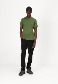 Green cotton t-shirt with short sleeves, black drawstring pants, and gray sneakers with a textured sole. Black cap completes the outfit.