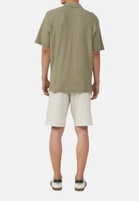Oliwkowa, krótko rękawowa, prążkowana koszulka polo zestawiona z białymi szortami, noszona z casualowymi butami, widziana z tyłu.