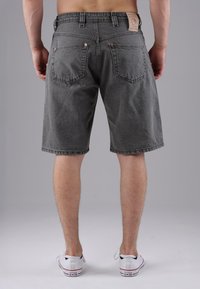 Man standing barefoot in gray denim shorts and white Converse sneakers, shown from the back against a plain background.