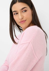 Helles rosa gestricktes Sweatshirt mit lockerem Muster, Rundhalsausschnitt und weiten Ärmeln. Der Stoff hat eine weiche, luftige Qualität.