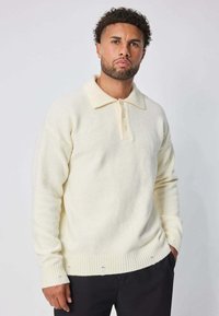 Pull polo de couleur crème en maille douce, avec un ourlet côtelé, trois boutons et un col structuré.