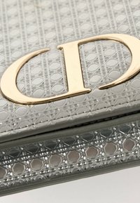 Portefeuille en cuir texturé gris avec un logo en métal doré comportant les lettres stylisées C et D sur le rabat avant.