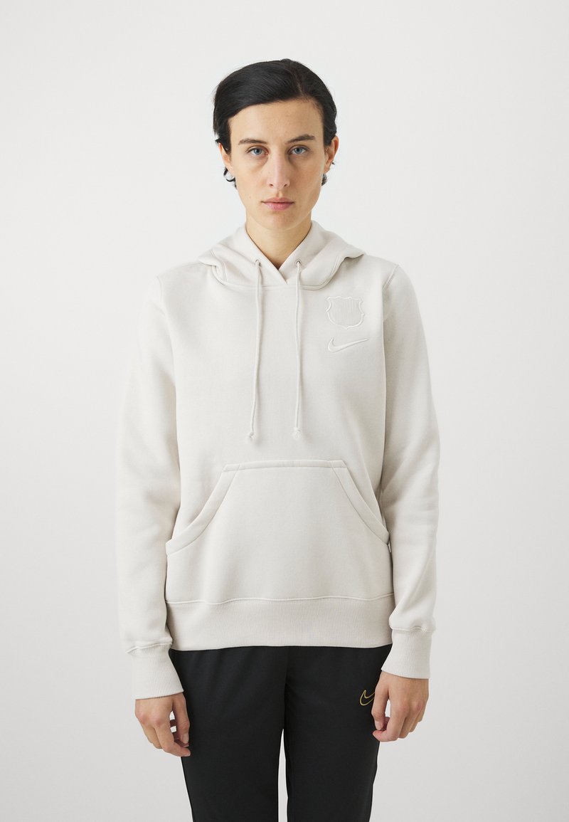 Hoodie crème avec une poche kangourou, des cordons de serrage et des détails de logo brodés. Tissu doux, coupe décontractée, associé à un pantalon noir.