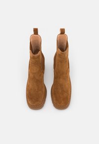 Botas de tobillo de ante marrón con un acabado suave, punteras redondas, paneles laterales elásticos y lengüetas para facilitar su uso. Suelas de goma planas.