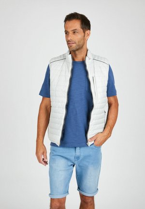 Light gray puffy vest with a high collar, zip closure, and subtle black accents, worn over a blue T-shirt and denim shorts.