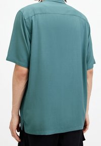 Korte mouwen overhemd in teal stof, met een ontspannen pasvorm, subtiele glans en zijsplitten aan de zoom voor extra bewegingsvrijheid.