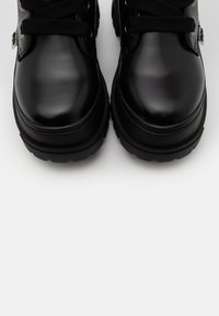 Paire de bottes en cuir noir brillant avec semelles épaisses et lacets noirs, vue de dessus sur fond blanc.