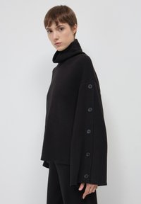 Maglione nero a collo alto con una vestibilità ampia, caratterizzato da grandi bottoni lungo una manica e una texture morbida.