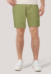 Pantaloni corti verde oliva in morbido cotone, con vestibilità standard, gamba dritta e orlo arrotolato, abbinati a sneakers bianche.