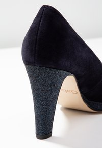 Mörkblå mocka högklackad sko med spetsig tå och en glittrande blå glitternagel, med en vadderad sula för komfort.