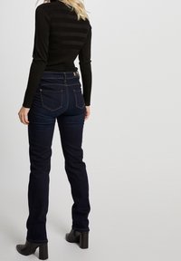 Donkere denim jeans met een slanke pasvorm, voorzien van een tailleband op middelhoge hoogte, achterzakken en stiksel details, gecombineerd met een zwart textuurtrui.