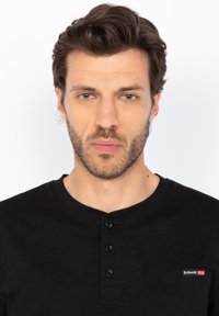 Maglietta nera in stile henley con colletto a girocollo, placca con tre bottoni e taschino sul petto con un accento di logo rosso e bianco.