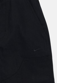 Černé sportovní kalhoty vyrobené z odolné látky, s bočními kapsami a decentním logem Nike v tmavě šedé barvě poblíž oblasti kapsy.