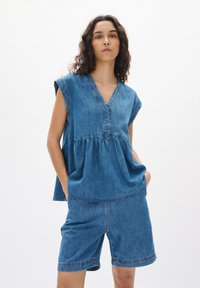 Gaiši zils denim peplum topiņš ar V veida kakla izgriezumu un īsām piedurknēm, apvienots ar atbilstošām džinsu šortiem, abiem ar smalkām šuvju detaļām.