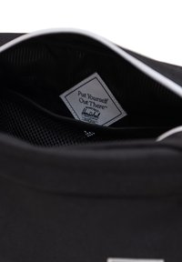 Interno di una borsa nera con un'etichetta bianca contenente testo, texture morbida e tasca in rete. L'etichetta mostra il nome del marchio e lo slogan in testo nero.