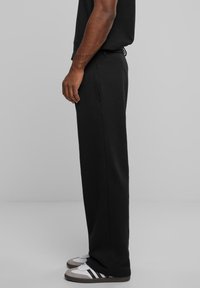 Pantalones deportivos negros de corte suelto, con bolsillos laterales y cinturilla elástica, combinados con zapatillas blancas y acentos grises.