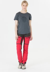 Grijs t-shirt met korte mouwen en een grafische print, gecombineerd met helderrode en donkergrijze broek met cargozakken en ritsen.